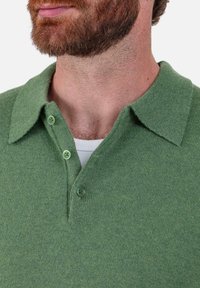 Polo vert en maille avec un col en V et trois boutons vert clair. Le tissu présente une texture douce et un motif chiné subtil.