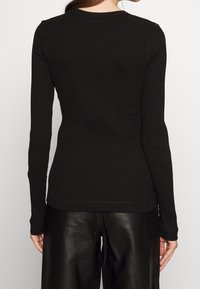 Top lungo a maniche nere in tessuto rigato con scollatura rotonda, dalla linea aderente e dalla texture semplice. Abbinato a pantaloni in pelle nera.