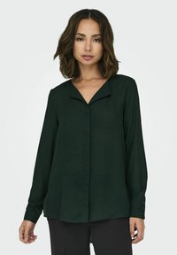 Blusa verde scuro a maniche lunghe con colletto a picco e polsini con bottoni; realizzata in tessuto liscio con una vestibilità rilassata e una leggera lucidità.