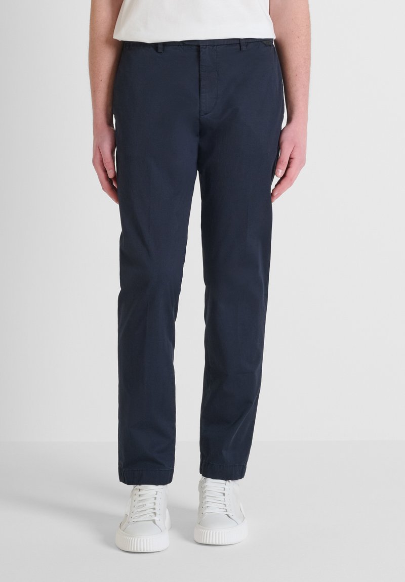 Pantaloni in cotone blu navy con taglio dritto, dotati di tasche laterali e chiusura con zip. Abbinati a sneaker bianche per un look casual.