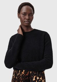 Mustat neulotut neuleet, joissa on pyöreä pääntie ja ribbauskainalot, yhdistettyinä laskostettuun hameeseen, jossa on erottuva abstrakti kuvio.