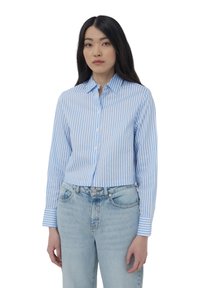 Camicia azzurra e bianca a righe, con colletto e maniche lunghe, abbinata a jeans in denim chiaro a vita alta.