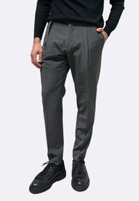 Pantaloni grigi su misura con una texture liscia. Presentano pince anteriori, tasche laterali e un taglio aderente. Abbinati a sneakers nere.