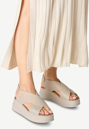 Sandali con zeppa beige dal design a strap incrociati, suola in gomma e finitura liscia. Dita dei piedi visibili e cinturino sul tallone regolabile.