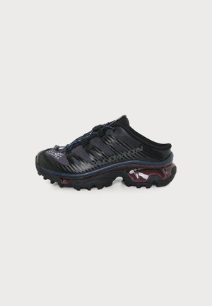 Chaussure de sport noire et violet foncé à enfiler, avec une semelle épaisse crantée, un système de laçage rapide, un texte de marque latéral et un détail de rembourrage.