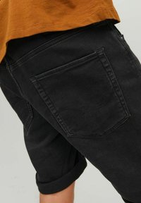 Bermude negre din denim cu un tiv răsucit, având un buzunar pe spate și cusături tonale. Țesătura are o textură netedă și un finisaj mat.