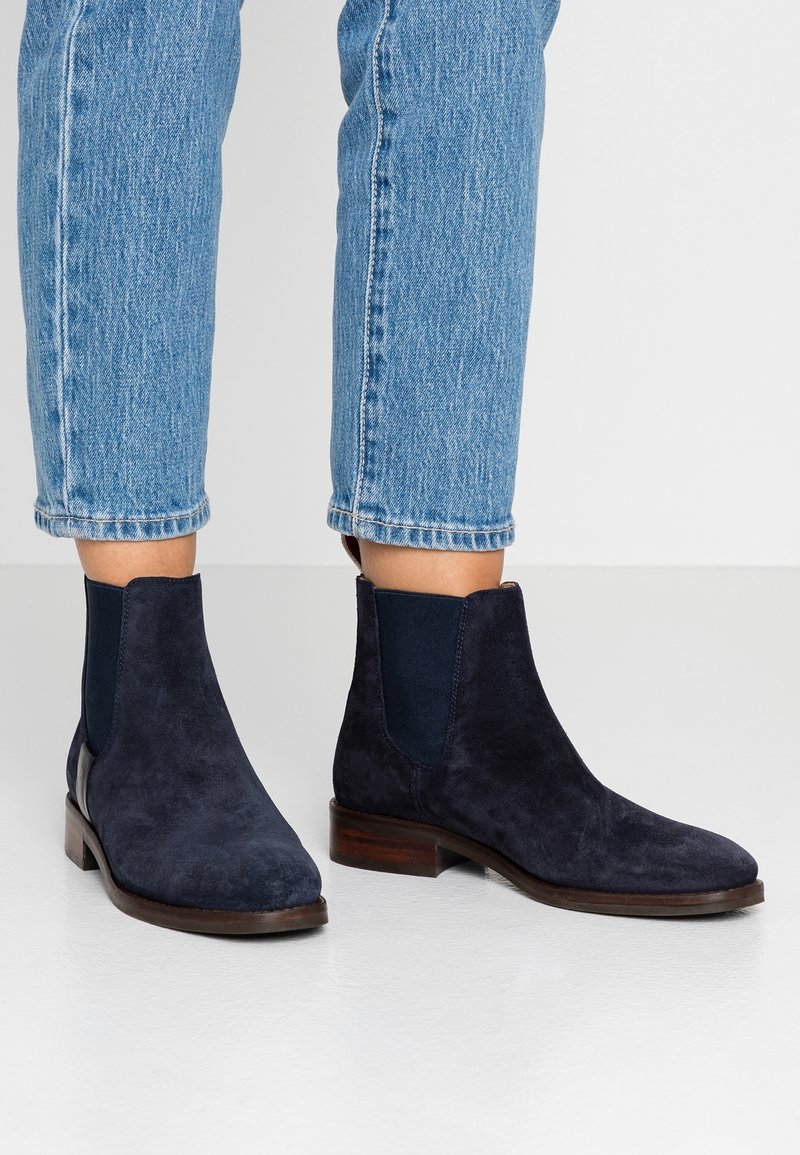 Marineblauwe suède enkellaarsjes met elastische zijkanten, een ronde neus en een houten gestapeld hak. Gecombineerd met cropped lichtblauwe jeans.