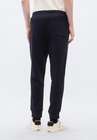 Μπλε ναυτικές φόρμες με ελαφρώς στενή γραμμή, ελαστική μέση και πίσω τσέπη. Φορεμένες με κρεμ αθλητικά παπούτσια με κορδόνια.