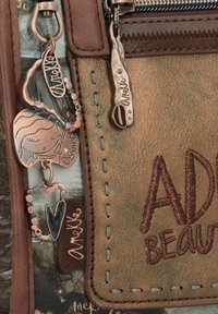 Sac en simili cuir marron avec une finition texturée, orné de pendentifs en métal décoratifs et de coutures. Comprend des détails colorés en perles.