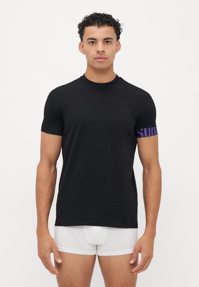 Schwarzes T-Shirt mit kurzen Ärmeln aus glattem Material, das ein lila Logo-Highlight am linken Ärmel besitzt. Klassischer runder Ausschnitt, taillierte Form.