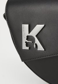 Borsa in pelle nera con logo K argentato, design della pattina angolato, texture liscia e dettagli cuciti.