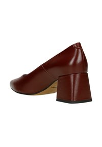 Chaussure en cuir marron avec un bout arrondi et un talon épais. La texture est lisse avec des coutures visibles le long des bords.