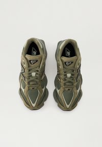 Sneakers oliivivihreänä, joissa on verkko- ja mokkanahkamateriaali, paksu, teksturoitu pohja, pyöreä kärki ja nauhakirjontajärjestelmä. Huomiota herättävät logovivahteet.