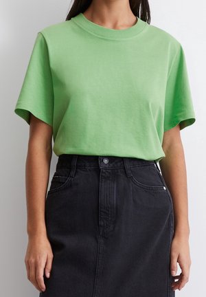 Zielona bawełniana koszulka o okrągłym dekolcie i krótkich rękawach, zestawiona z wysokim stanem czarnej spódnicy jeansowej z przednim zapięciem na guziki i kieszeniami.