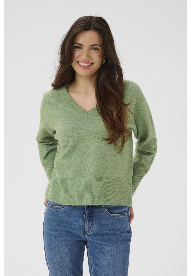 Pull léger vert clair à col en V en maille douce, avec ourlet et poignets côtelés, associé à un jean en denim bleu. Design simple.