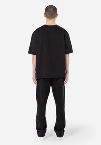 Tricou oversized negru, cu mâneci scurte și guler rotund, asortat cu pantaloni de trening negri. Design minimalist, cu o textură moale.
