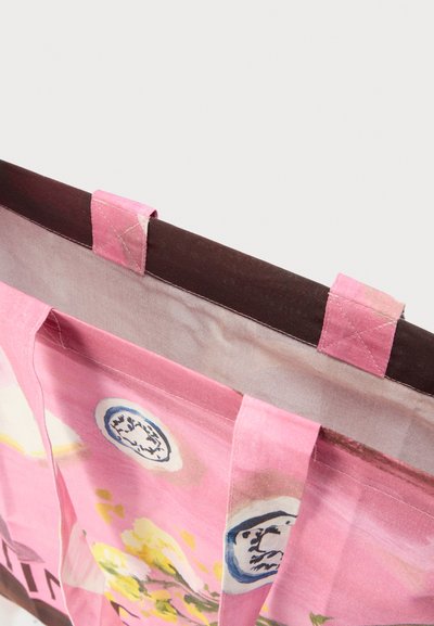 Κοντινό πλάνο ροζ υφασμάτινης τσάντας tote με λουλουδάτα και κυκλικά μπλε σχέδια, με ραμμένες λαβές και καφέ εσωτερική επένδυση.