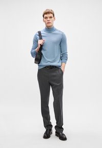 Απαλή μπλε πλεκτή ζακέτα με ψηλό λαιμό, γκρι παντελόνι, μαύρη ζώνη και μαύρη τσάντα. Λείο υλικό, εφαρμοστή σχεδίαση και μινιμαλιστικές λεπτομέρειες.