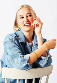 Giubbotto di jeans con una vestibilità rilassata, colore azzurro chiaro, indossato sopra una maglietta bianca. La modella indossa un braccialetto con motivo verde e giallo e orecchini a cerchio.