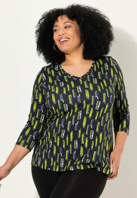 Svart topp med V-ringning och trekvartsärmar. Mönstret har vertikala gröna, blå och vita ränder på en mörk bakgrund. Mjuk tyg.