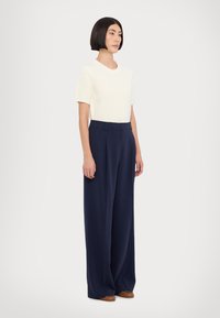 Haut crème à manches courtes avec texture côtelée associé à un pantalon large taille haute bleu marine. Des chaussures brunes complètent la tenue.