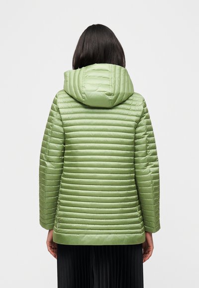 Personne aux cheveux noirs mi-longs portant une veste matelassée vert clair avec capuche, vue de dos sur un fond uni.