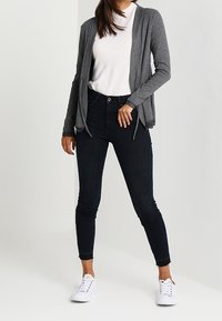 Šedý lehký kardigan přes bílý top, spárovaný s tmavými skinny džíny a bílými teniskami. Uvolněný střih s příležitostním vzhledem.