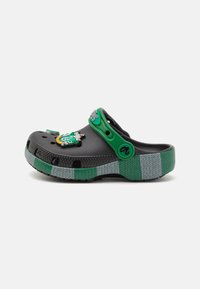 Black clog with a green strap and accents, featuring a textured gray and green striped sole. Includes decorative elements on the front.