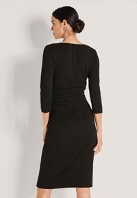 Zwarte jurk met driekwart mouwen, getailleerde silhoe t en een geraffineerd detail aan de achterkant. Gladde textuur met subtiele glans.