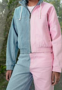 Džínová bunda s kontrastními světle modrými a růžovými částmi, vybavená zipem, kapucí se stahovací šňůrkou a elastickým pasem.