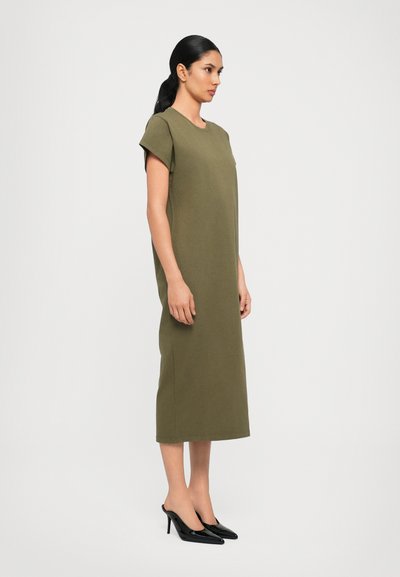 Olive green, knee-length dress with short sleeves and a round neckline. Paired with black high-heeled shoes. Smooth fabric texture.
