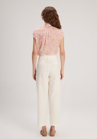 Blusa a maniche corte di un delicato colore rosa con un motivo floreale; abbinata a pantaloni bianchi a vita alta con gamba larga e sandali piatti marroni.