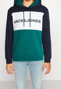 Sudadera con capucha de diseño a bloques de color en azul marino, verde azulado y blanco. Presenta cordones y un gran logo en la parte frontal. Tejido suave.