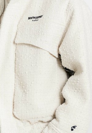 Gestructureerd wit jack van zachte stof, met een opvallende borstzak en geborduurd merklogo in zwart op de schouder.