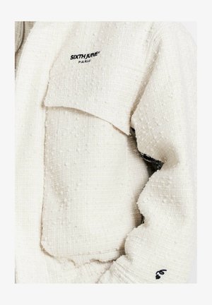 Gestructureerd wit jack van zachte stof, met een opvallende borstzak en geborduurd merklogo in zwart op de schouder.