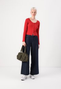 Cardigan rouge à rayures côtelées à manches longues avec un décolleté en bateau, associé à un jean en denim foncé à jambes larges. Sac à main vert olive avec poches avant et poignées courtes.