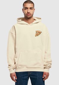 Hoodie boje kreme s prednjim džepom, s grafikom kriške pizze na lijevoj strani prsnog koša. Izrađen od mekanog materijala. Opušteni kroj.