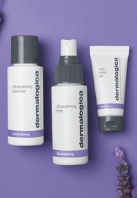 Tre prodotti per la cura della pelle Dermalogica: un detergente ultracalming bianco, un spray in una bottiglia ghiacciata con un tappo a spruzzo nero e un gel calmante in un tubo bianco, tutti esposti su uno sfondo viola.