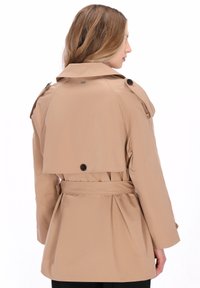 Bézs színű ballonkabát öves derékrésszel, gombos díszítéssel és élénkített, redős hátkialakítással. Nagy gallérral és vállpántokkal rendelkezik.