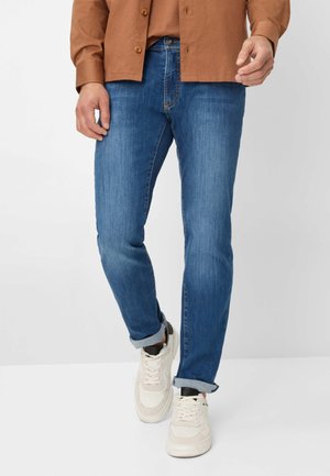 Blauwe denim jeans met een slim fit. Ze hebben een lichte vervaging en opgerolde boorden, gecombineerd met witte sneakers en een bruine button-up shirt.