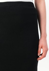 Gonna nera a maglia con una texture liscia e una vita elasticizzata, design aderente, con cucitura piatta in vita e spacchi laterali.