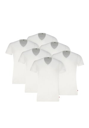 Mann trägt ein schlichtes weißes V-Neck-T-Shirt und graue Boxershorts, steht vor einem einfarbigen hellen Hintergrund.