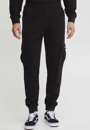 Svarte cargo-svet pants laget av mykt stoff, med to sidelommer og elastiske mansjetter. Kombinert med svart-hvite joggesko.