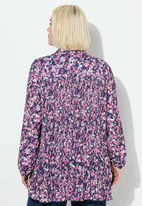 Blusa floral en azul marino con estampados en rosa y blanco, detalle plisado en la espalda, mangas largas y un ajuste holgado. Confeccionada con tela ligera.