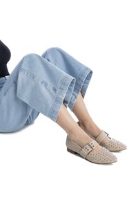 Zapatos beige con tachuelas, con una correa con hebilla, punta afilada y tacón bajo, combinados con pantalones de mezclilla cortos de color azul claro. Textura de cuero suave.