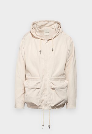 Jasno beżowa kurtka z kapturem, ze sznurkiem, dwoma przednimi kieszeniami, długimi rękawami i zamkiem błyskawicznym. Gładka tekstura materiału.