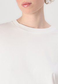 Weißes Baumwoll-T-Shirt mit rundem Halsausschnitt und kurzen Ärmeln, mit glatter Textur und ohne sichtbare Muster oder Akzente.