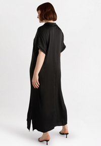 Schwarzes Satin-Kleid mit einer langen, lockeren Passform, kurzen Ärmeln, einem Kragen und seitlichen Schlitzen. Geschmeidige Textur mit minimaler Detailierung.