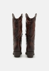 Botas de cuero marrón hasta la rodilla con textura de patrón de cocodrilo, un diseño superior abierto y un pequeño tacón. Presentan un sutil diseño de costuras y una cremallera lateral.