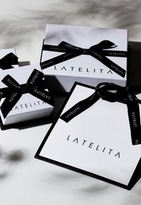 Tre hvide gaveæsker med sorte bånd. Den største æske har fed sort skrift "LATELITA." Enkel, moderne design med mat finish.